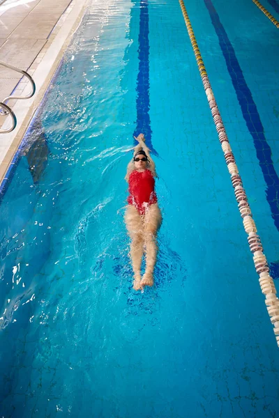 穿着护目镜和泳帽的职业女运动员在游泳池里漂浮在她的背上 — 图库照片