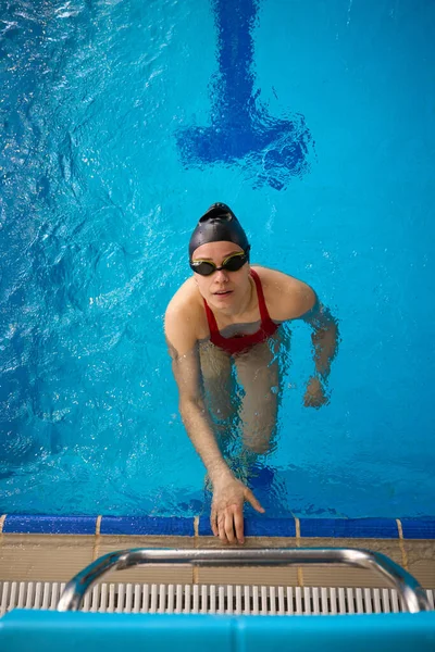 Top view of swimmer in swim cap and goggles standing in water and looking up at camera