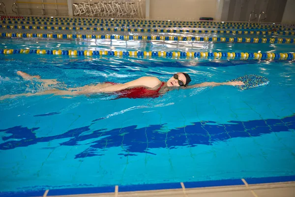 身穿护目镜 头戴安全帽的女运动员一边带着踢脚板一边游泳 — 图库照片