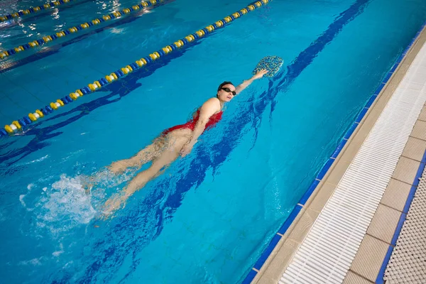 キックボードで水で運動中の水泳キャップとゴーグルでのスポーツウーマンのトップビュー — ストック写真