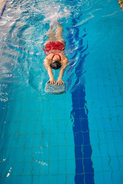 両手でキックボードを保持しながらプールで胃に浮かぶ水泳者のトップビュー — ストック写真