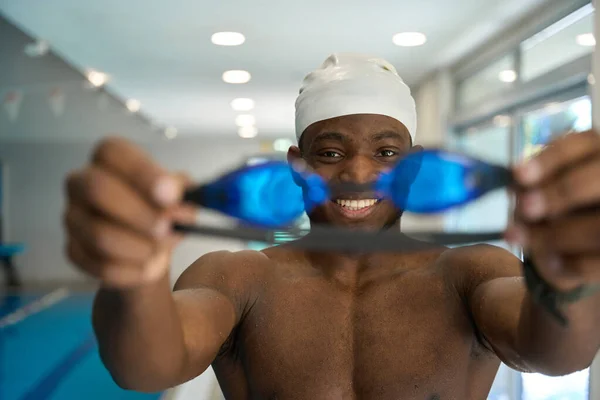 Portrait of cheerful young swimmer holding swim goggles in front of camera