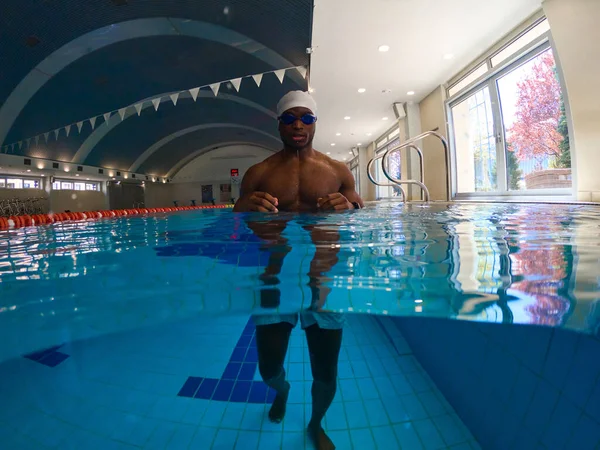 Fit young swimmer in swim cap and cyan goggles standing in water