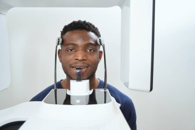 Amerikalı adam klinikte bilgisayarlı tomografi cihazının yanında oturuyor. Kafatası ve dişlerin tomografik görüntüsü