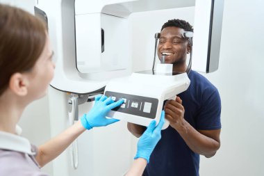 Erkek klinikte bilgisayarlı tomografi cihazının yanında duruyor. Kafatası ve dişlerin tomografik görüntüsü