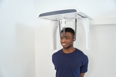 Hasta klinikte bilgisayar tomografi cihazının yanında duruyor. Kafatası ve dişlerin tomografik görüntüsü