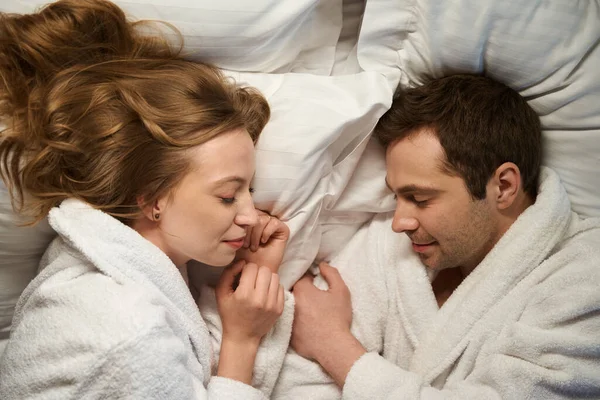 Beautiful couple falling asleep in warm bathrobes after spa procedures and recreational pursuit, husband and wife spending weekend together at hotel resort