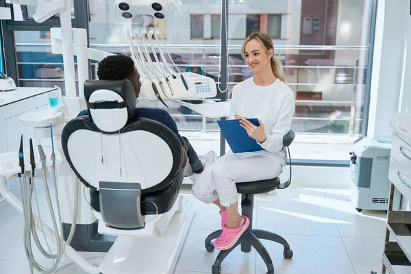 Usmívající Žena Zubní Technik Poslouchat Klienta Dělat Lékařské Záznamy Sedí — Stock fotografie