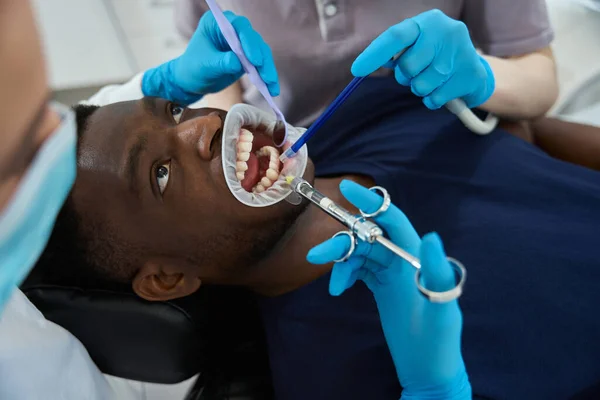 女性の歯科医は男性の顧客に口の引き込み器を挿入し 歯の処置 根管療法または歯の抽出の前に麻酔注入をする — ストック写真