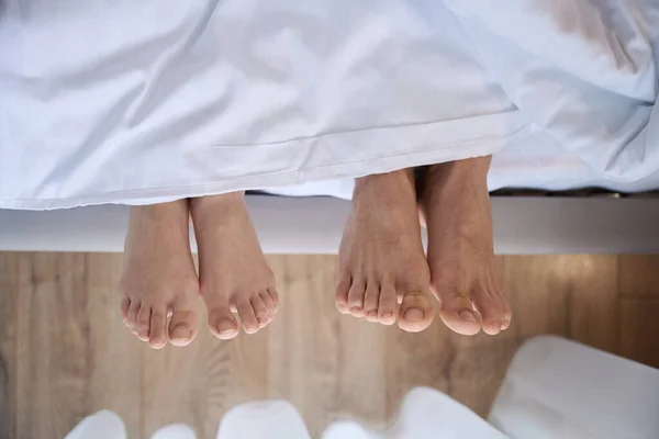 Close up of two pairs of feet looking from under white blanket