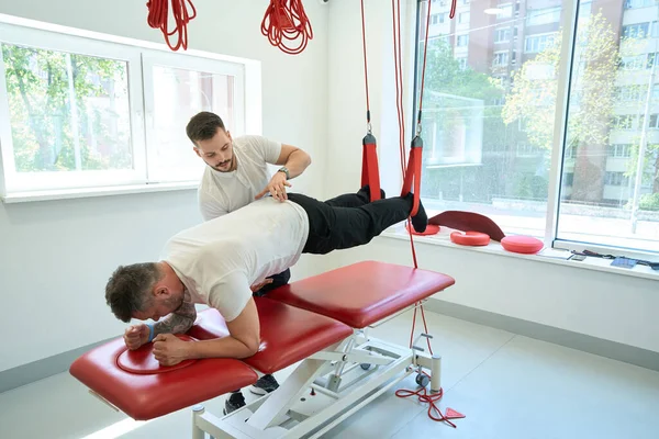 Konzentrierte Physiotherapeutin Hilft Patientin Bei Anfälliger Überbrückungsübung Auf Suspension Trainer — Stockfoto