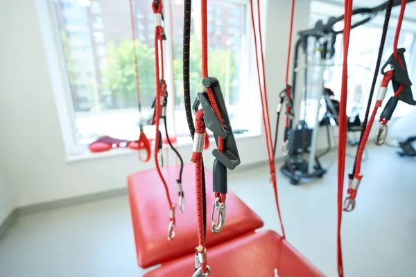 Suspension trainer with red straps and slings among other fitness machines in exercise room