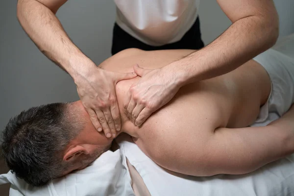 Cropped photo of man lying prone while masseur relaxing tight his upper back and neck muscles