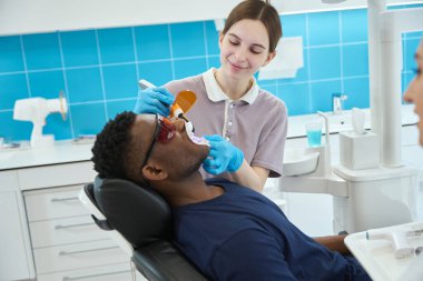 Koruyucu eldivenlerle gülümseyen kadın hemşire erkeğin yanında duruyor ve hastanede ultrasonik diş temizliği yapıyor.