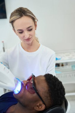 Hastanın yanında duran genç hemşire, gözlüklü adam sandalyede oturuyor ve klinikte tedavi görüyor.