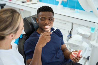 Sandalyede oturan ve elinde maket olan genç bir erkek. Koruyucu eldivenli bir doktor.