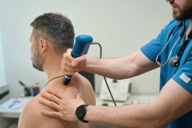 Cropped photo of adult man undergoing extracorporeal shockwave therapy session for upper back pain clipart