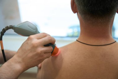 Doktorun elinin üst trapezius tetikleme noktasındaki lazer ışınını yetişkin kişide yönlendirmesi.