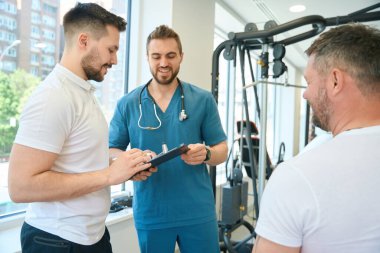 Neşeli doktor antrenörüne antrenörlüğünü spor salonunda müşterisinin önünde yapıyor.
