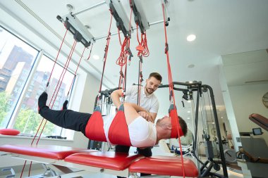 Erkek, doktor destekli askı egzersizi seansı sırasında kas aktivasyonu yapıyor.