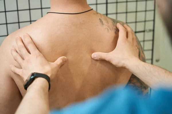 Cropped photo of physical therapist palpating male patient paravertebral muscles in upper back region