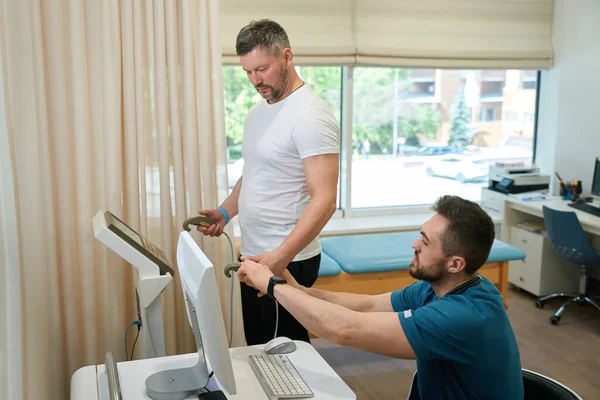 Adult person undergoing body composition analysis on analyzer with help of healthcare worker