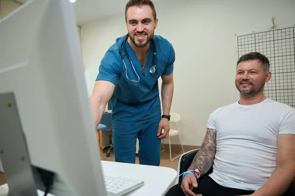 Usmívající Zdravotnický Pracovník Zaznamenávající Počítačový Elektrokardiogram Mužského Pacienta Poloze Vsedě — Stock fotografie