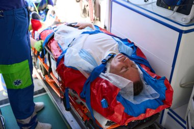 Sedyedeki hasta ambulansa bindiriliyor, deneyimli sağlık görevlileri ona serum takıyor.