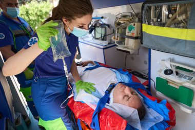 Hasta ambulansta sedyede yatıyor, deneyimli sağlık görevlileri onu seruma bağladı.