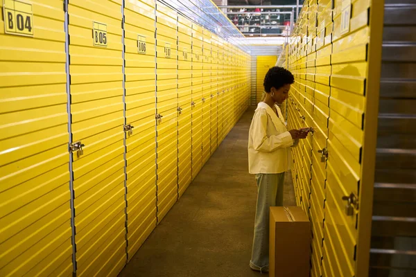 Young woman opening the lock on a storage unit, containers in a yellow warehouse