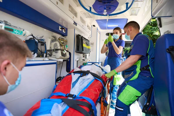 Paramedic woman puts a dropper with painkillers on the patient, a team of doctors transports a patient with polytrauma
