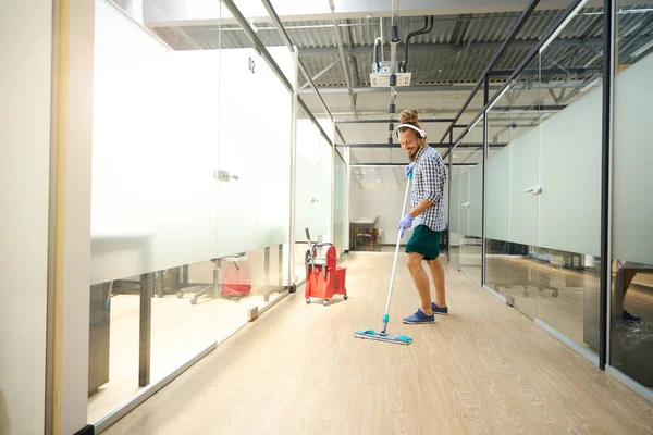 Informal cleaner washes the floor in the office corridor, he works to music, uses a headset