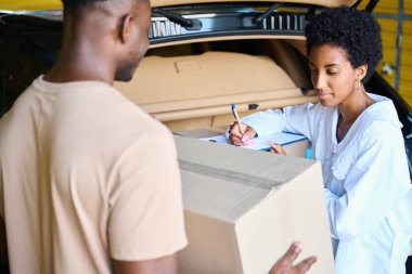 Afro-Amerikalı kadın yöneticiler, elinde karton kutu olan bir adamın yanında depolanan şeylerin envanterini çıkarıyorlar.