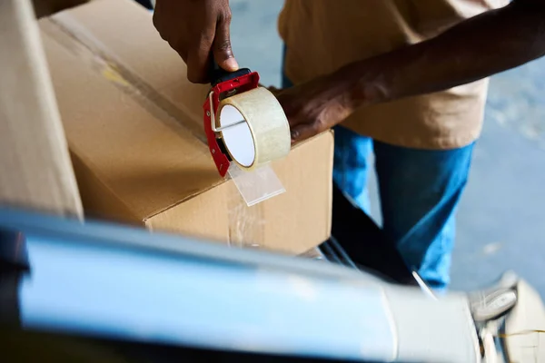 Man seals a cardboard box with tape, he uses a tape dispenser