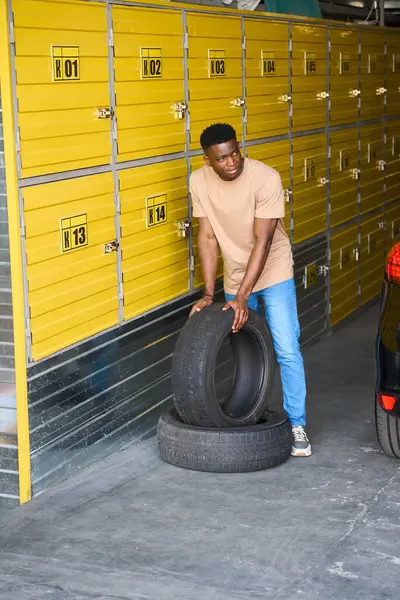 African American car driver brought wheels for seasonal storage, he unloaded car tires from the trunk