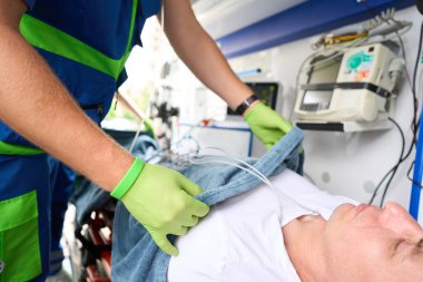 Paramedikler ambulansta yumuşak battaniyeli bir hastaya bakar, hasta özel bir sedyede yatar.