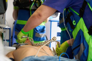 Doktor defibrilatör elektrotlarını hastanın gövdesine uyguladı. Hastanın canlandırmasını ambulansta yapıyor.