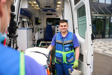 Sağlık görevlileri ambulansın yanında bekliyor, biri boyunluk tutuyor.