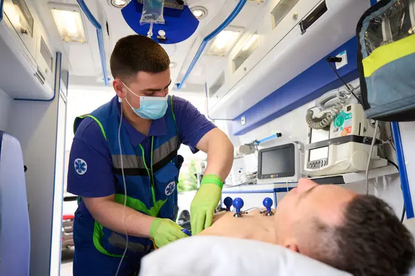 Paramedic attaches electrodes on suction cups to the torso of a man in an ambulance to take a cardiogram