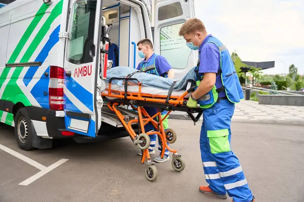 Colegas Paramédicos Descargan Una Camilla Con Paciente Una Ambulancia Coche — Foto de Stock