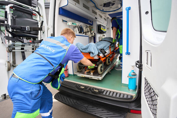 Loading a stretcher with a patient into a modern ambulance, paramedics work in protective gloves