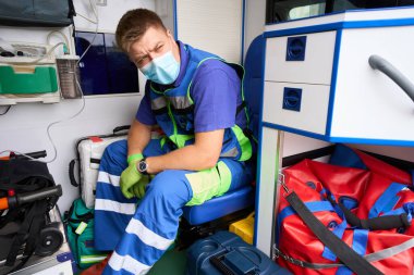 Koruyucu maskeli sağlık görevlisi ambulansta, arabanın modern ekipmanları var.