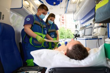 Doktorlar modern bir ambulanstaki bir adama kardiyogram yapar, hasta özel bir sedyede yatar.