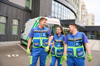 Ziyaretçi ekibinin doktorları modern bir binanın yakınındaki alanda yürüyor, yakınlarda bir ambulans var.