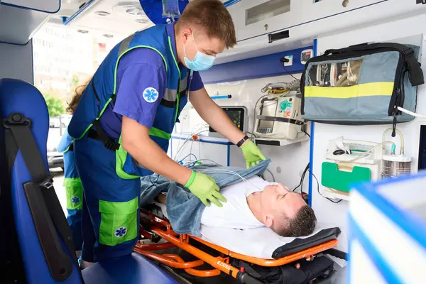 Koruyucu Eldivenli Bir Adam Ambulansta Yumuşak Battaniyeli Bir Hastayı Örtüyor — Stok fotoğraf