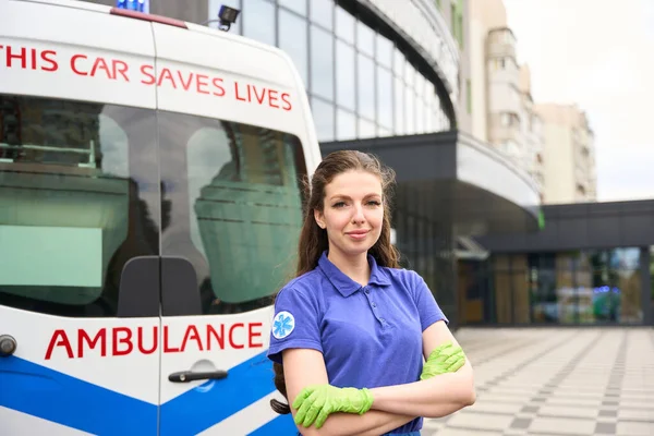Female medic stands on the street near an ambulance, she has a medical emblem on her sleeve