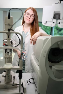 İş yerindeki sevimli kızıl saçlı göz doktoru, modern cihazlarla iç mekanda.