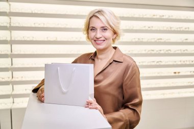 Bir paket içinde satın alma ile bir optik salonun gülen müşterisi, kuaförde geniş bir çerçeve seçimi