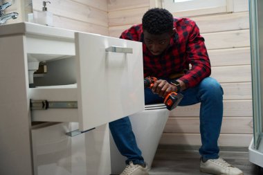 Male worker makes minor renovations in the bathroom, he uses his tool kit clipart