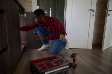 Genç tamirci bir eko-kulübede küçük tamiratlar yapıyor, alet çantasını kullanıyor.